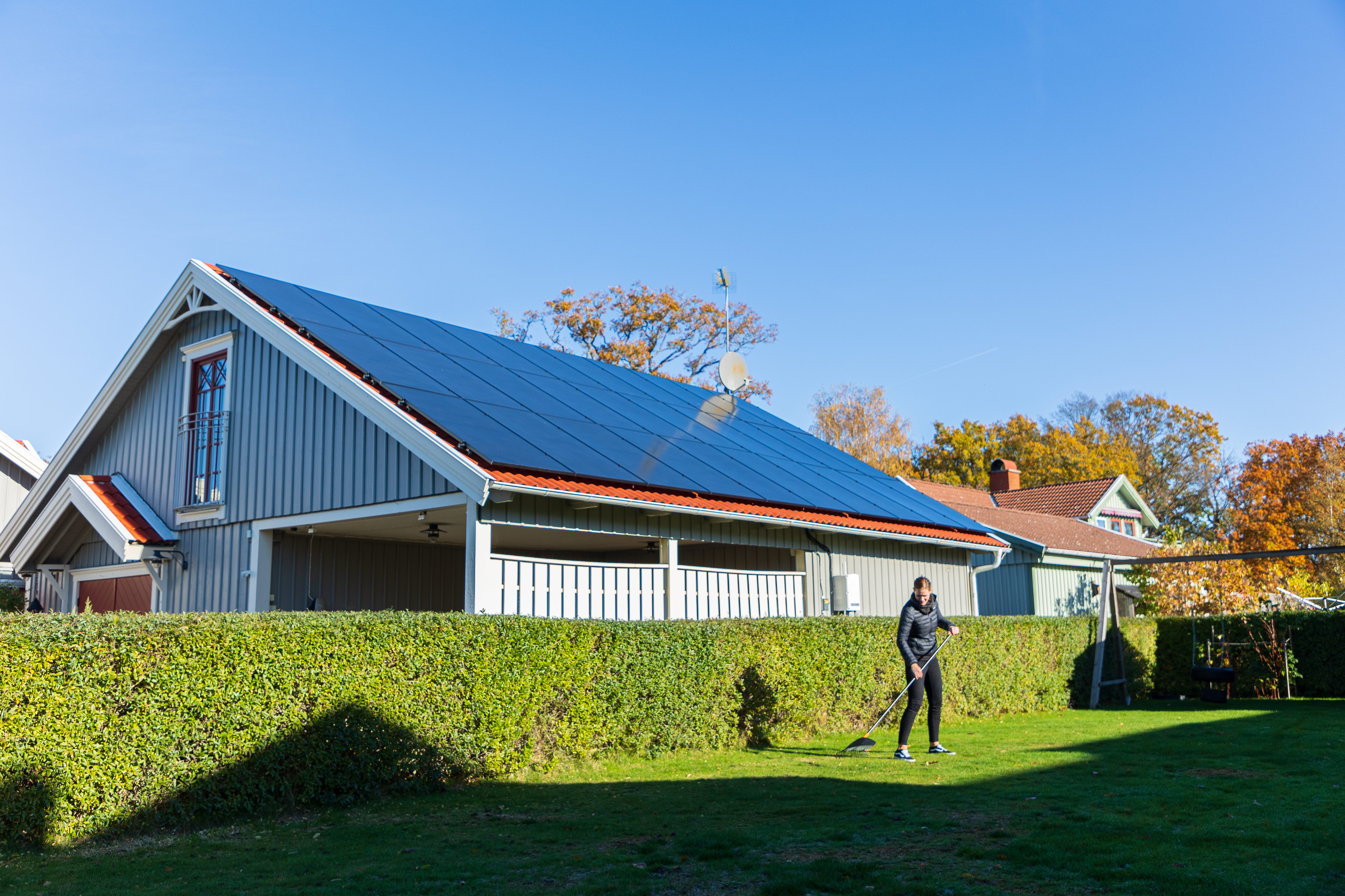 Villa med solceller på taket med en person som krattar framför