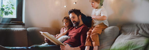 Pappa och barn läser bok i soffa.