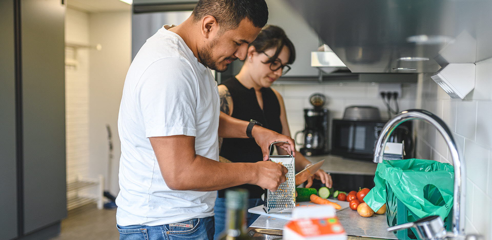 Två unga vuxna lagar mat i ett studentkök med gröna påsen redo