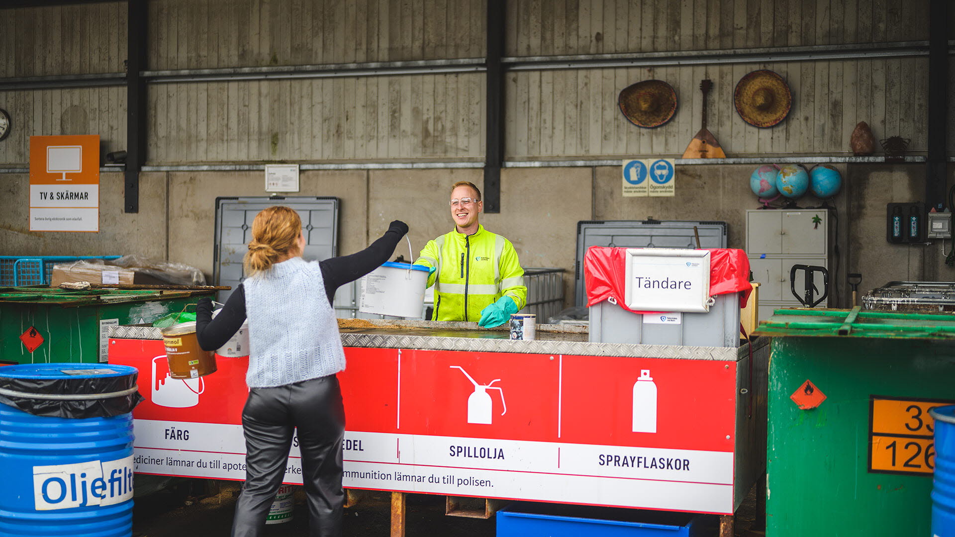 En kvinna lämnar över målarfärgsburkar till en medarbetare på Tekniska verken vid stationen för farligt avfall.