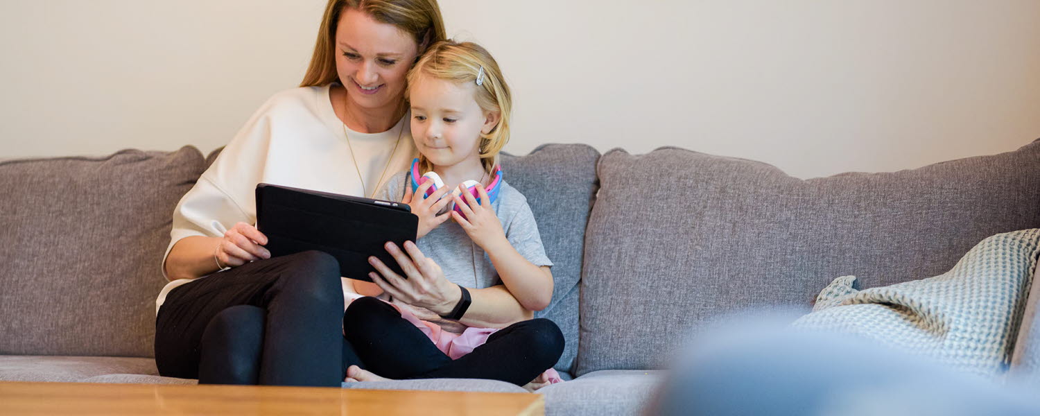 Mamma och dotter sitter i soffan och tittar på en padda tillsammans