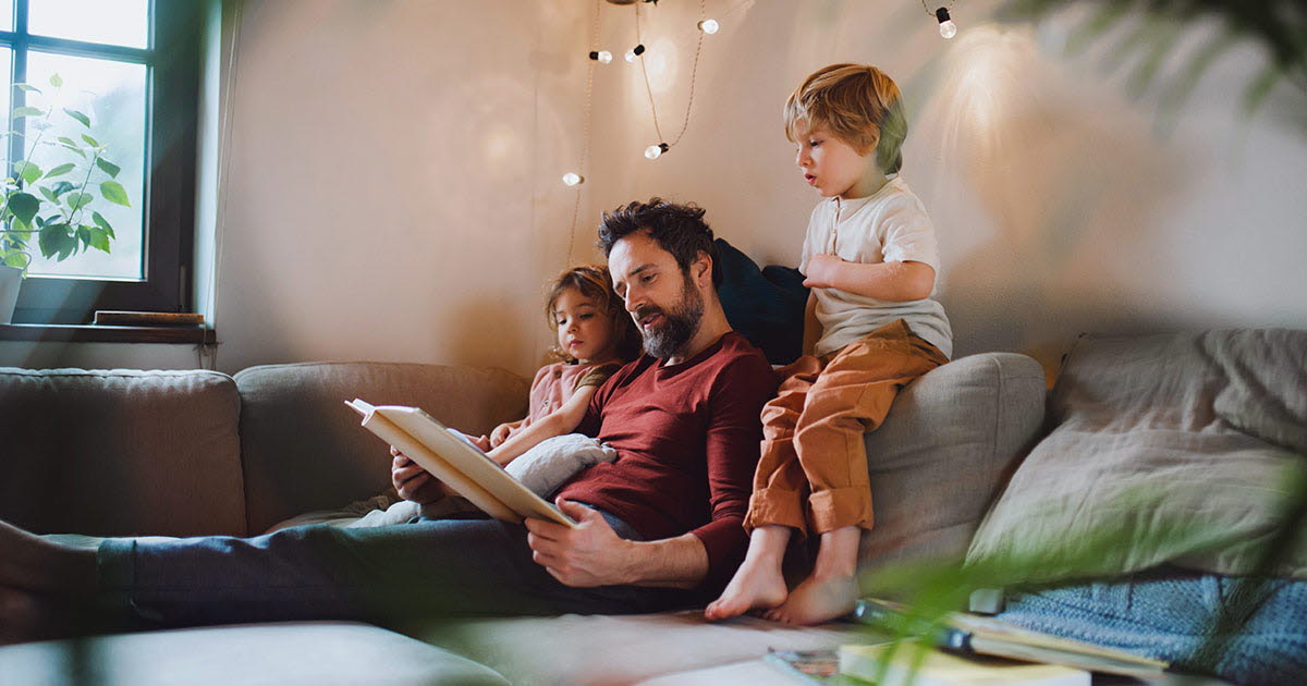 Pappa och barn läser bok i soffa.