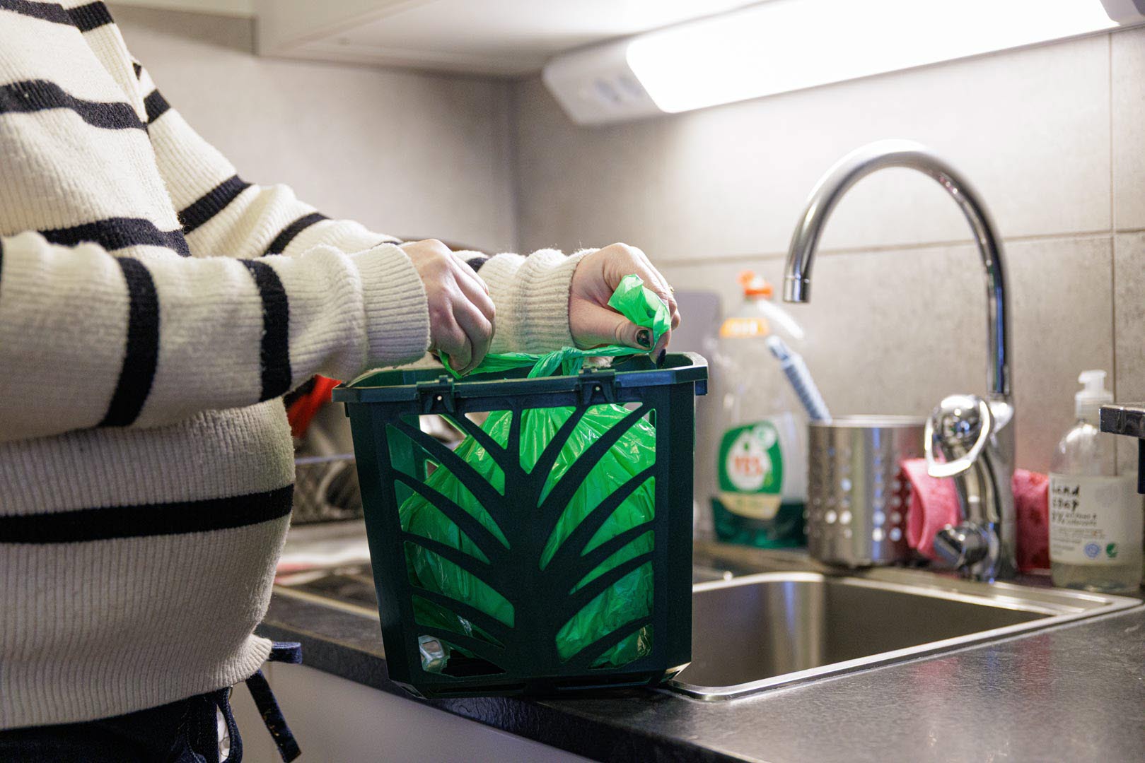 Närbild av en kvinna som tar upp gröna påsen ur en påshållare.